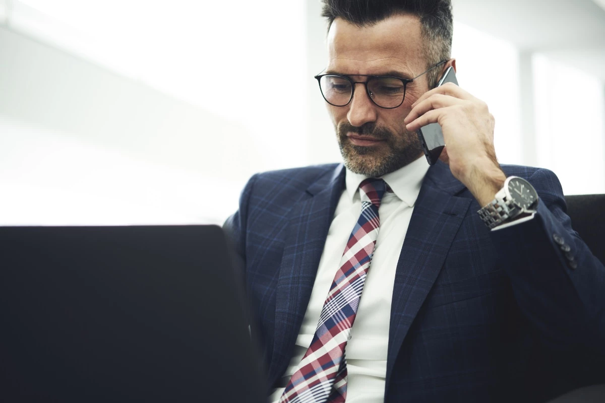 Manager bei der Arbeit am Laptop mit Handy am Ohr