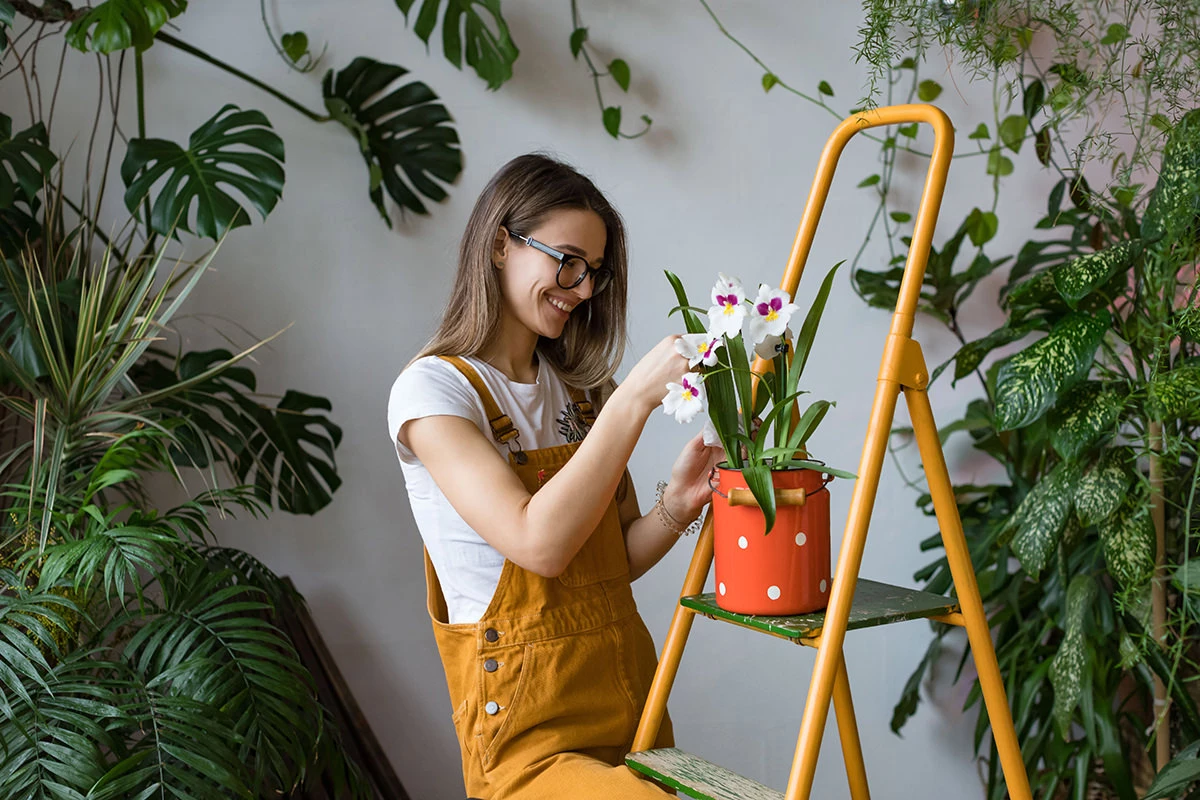 Junge Frau in einer Latzhose verschönert ihre Wohnung mit grünen Pflanzen.