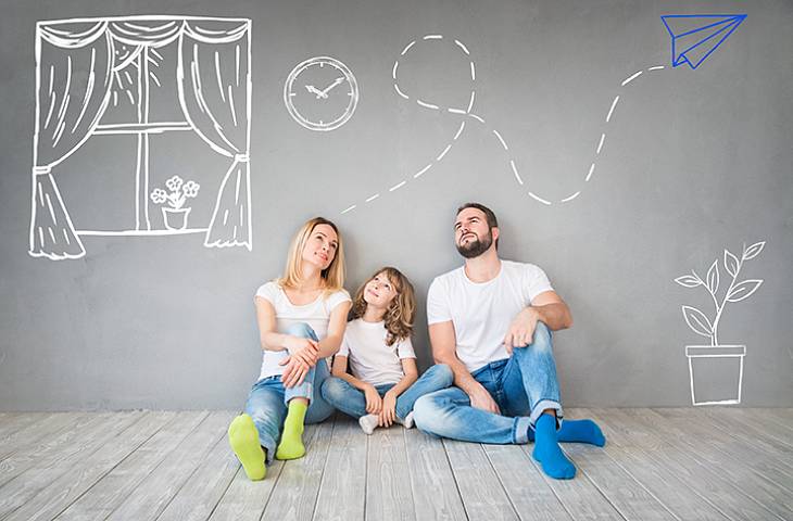 Familie sitzt in ihrer Wohnung auf dem Boden, an die Wand sind Fenster und ein Papierflieger gemalt.