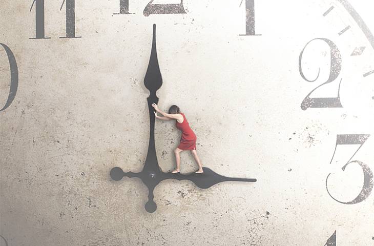 Riesige Uhr bei welcher eine Frau auf dem Stundenzeiger, der auf drei Uhr zeigt, steht und den Minutenzeiger in Richtung der 12 schiebt.