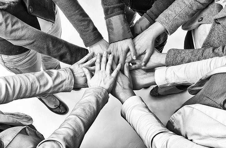 Mehrere Menschen stehen im Kreis und legen die Hände zusammen.