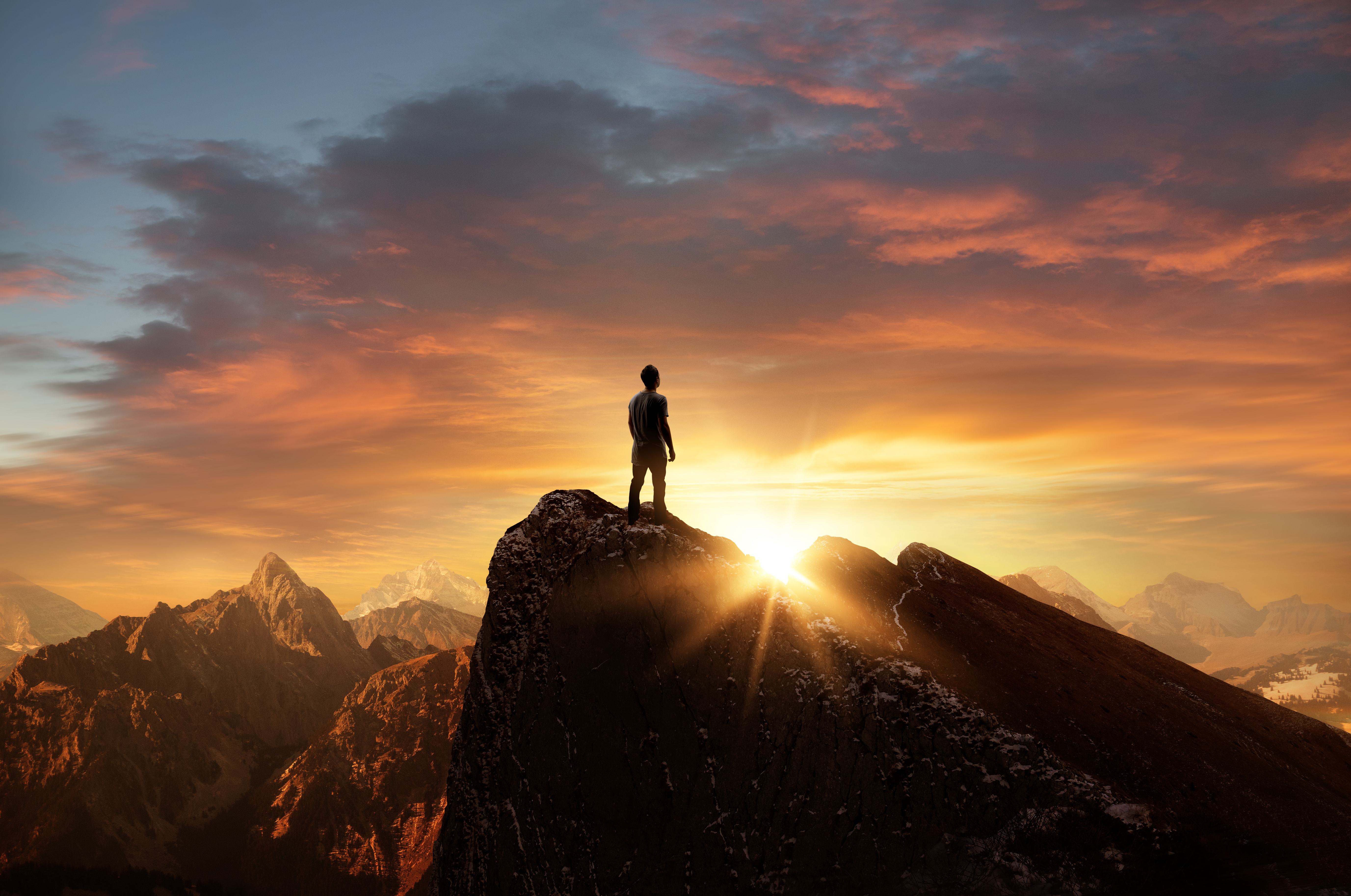 Mann steht auf einer Bergspitze und blickt Richtung Horizont entgegen der Sonne