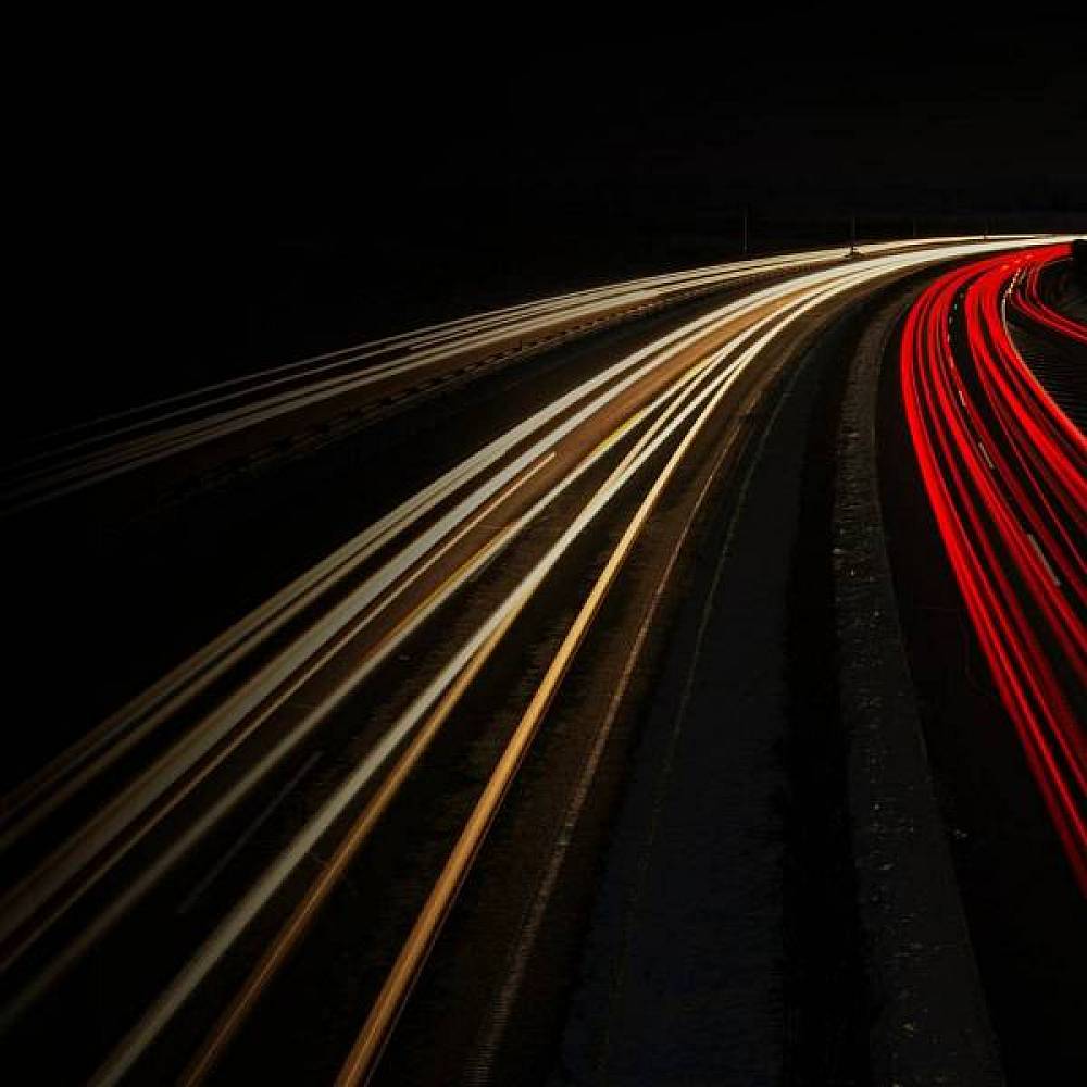 Langzeitaufnahme einer Autobahn bei Nacht mit Lichtmalerei durch vorbeifahrende Autos.