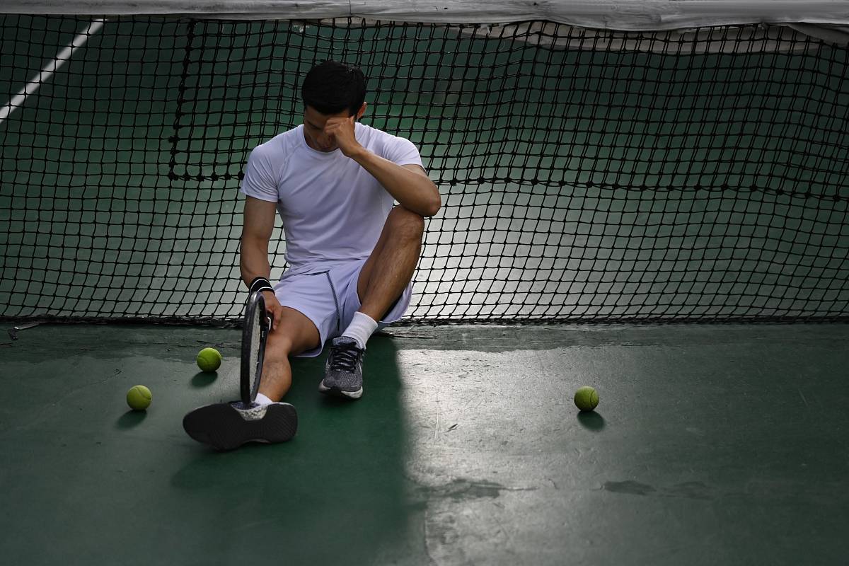Frustrierter Tennisspieler sitzt am Boden