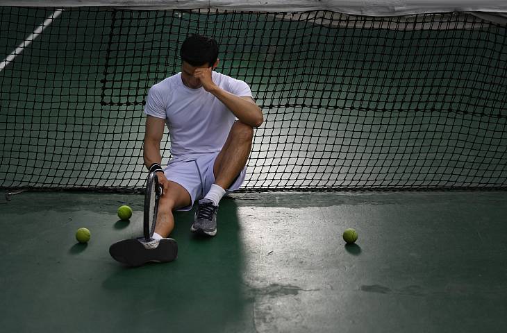 Frustrierter Tennisspieler sitzt am Boden