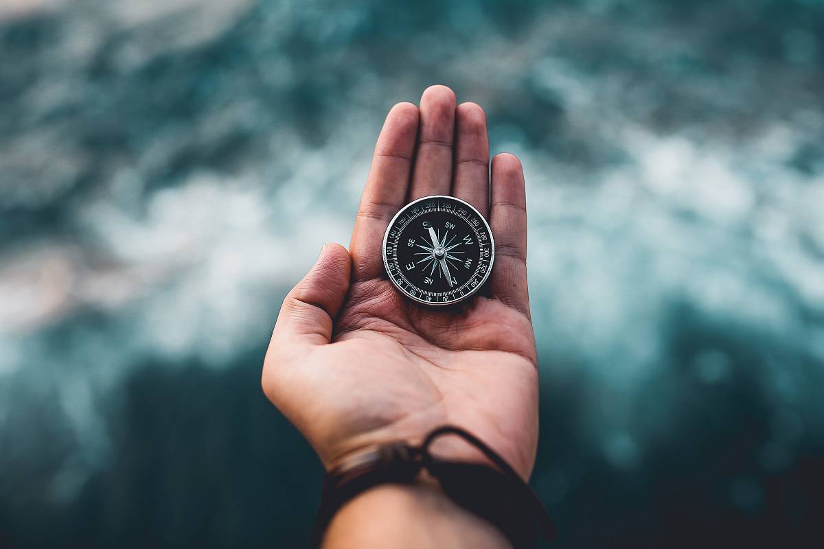 Eine ausgestreckte Hand hält einen Kompass vor einem rauen Meer – Symbol für Führung, Orientierung und den Weg durch Herausforderungen.