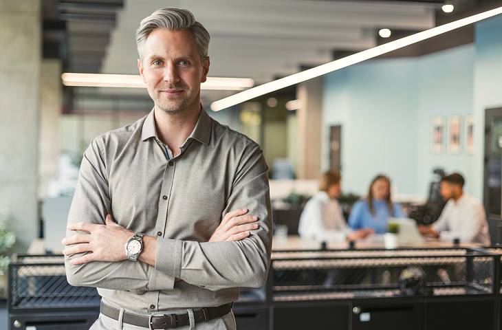 Geschäftsführer steht im Büro und blickt in die Kamera. Modernes Büro.