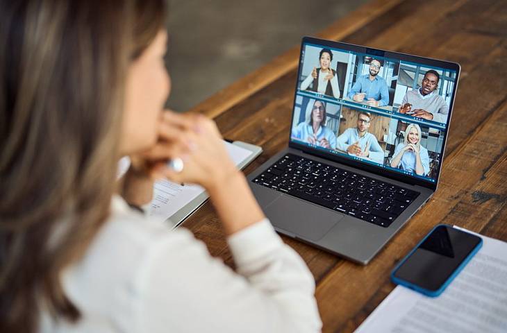 Frau sitzt am Schreibtisch und nimmt per Laptop an einer Videokonferenz mit mehreren Teilnehmern teil