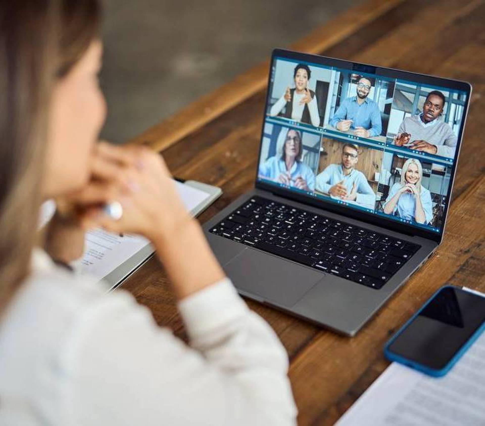 Frau sitzt am Schreibtisch und nimmt per Laptop an einer Videokonferenz mit mehreren Teilnehmern teil