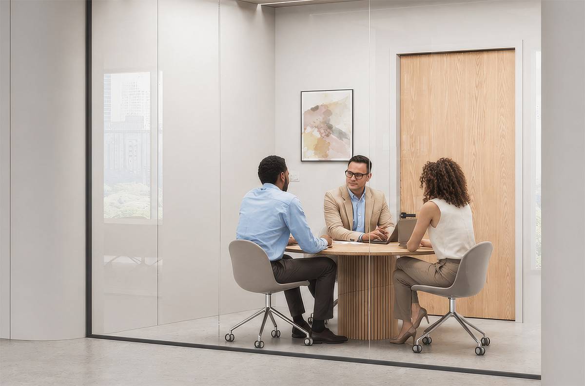 Drei Personen im persönlichen Beratungsgespräch in einem modernen, verglasten Besprechungsraum.